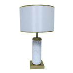 White marble cylinder table lamp with brass metal base and brass trim fabric shade turned off on white background