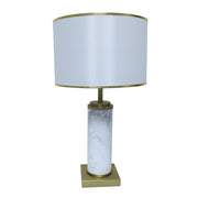 White marble cylinder table lamp with brass metal base and brass trim fabric shade turned off on white background