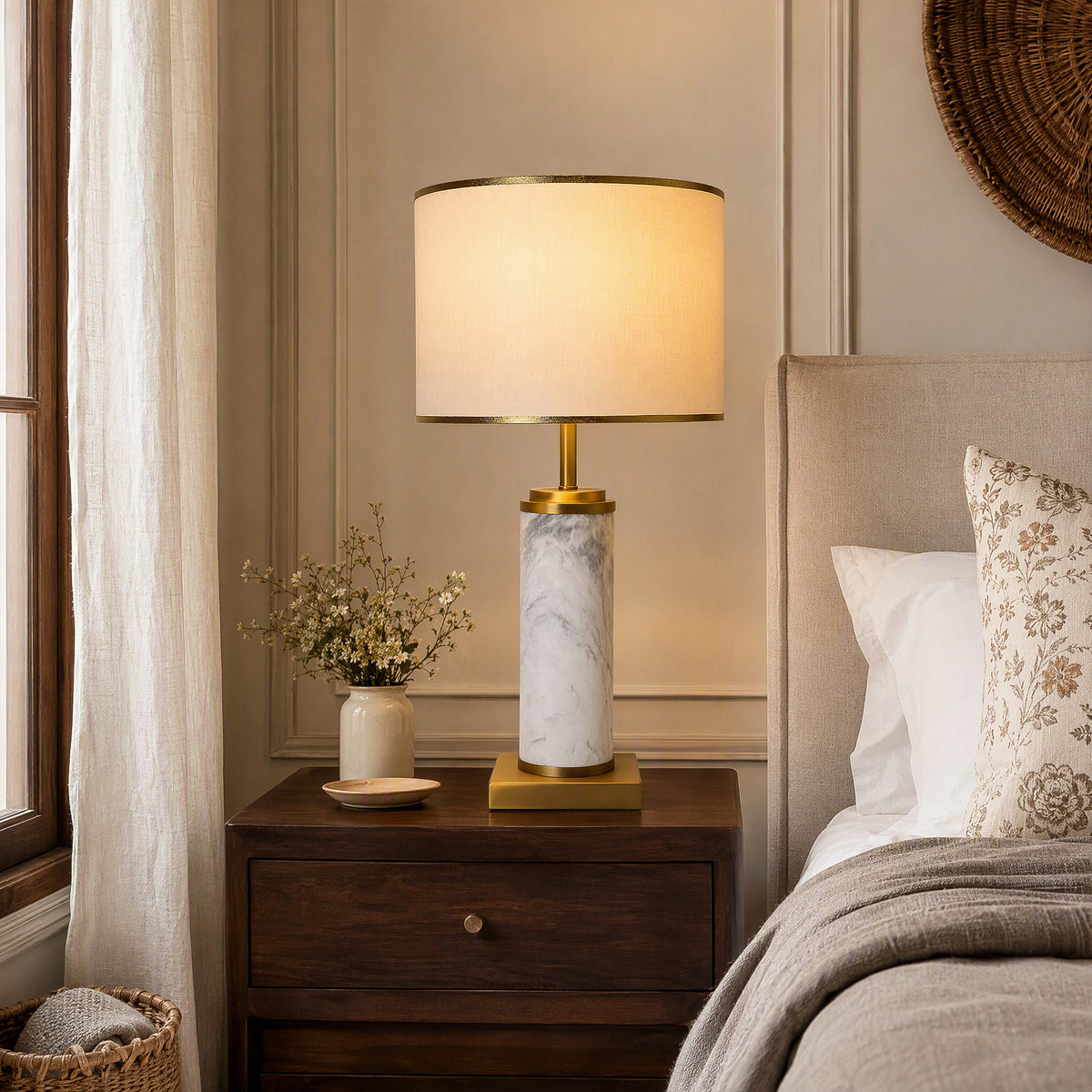 Illuminated white marble table lamp glowing warm light on dark wooden nightstand by modern bed